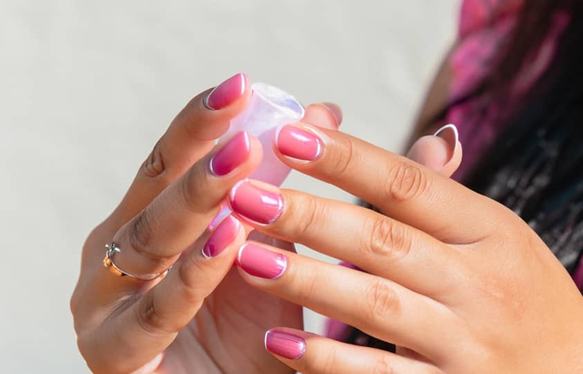 Une femme tient une bouteille de vernis à ongles rose.