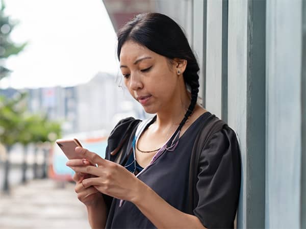 Une femme appuyée contre un mur regarde son téléphone.